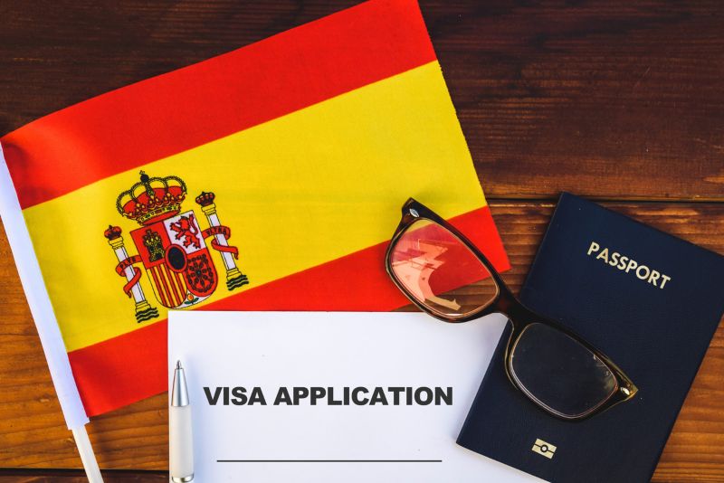 Spanish flag, passport and generic visa application paperwork on a desk